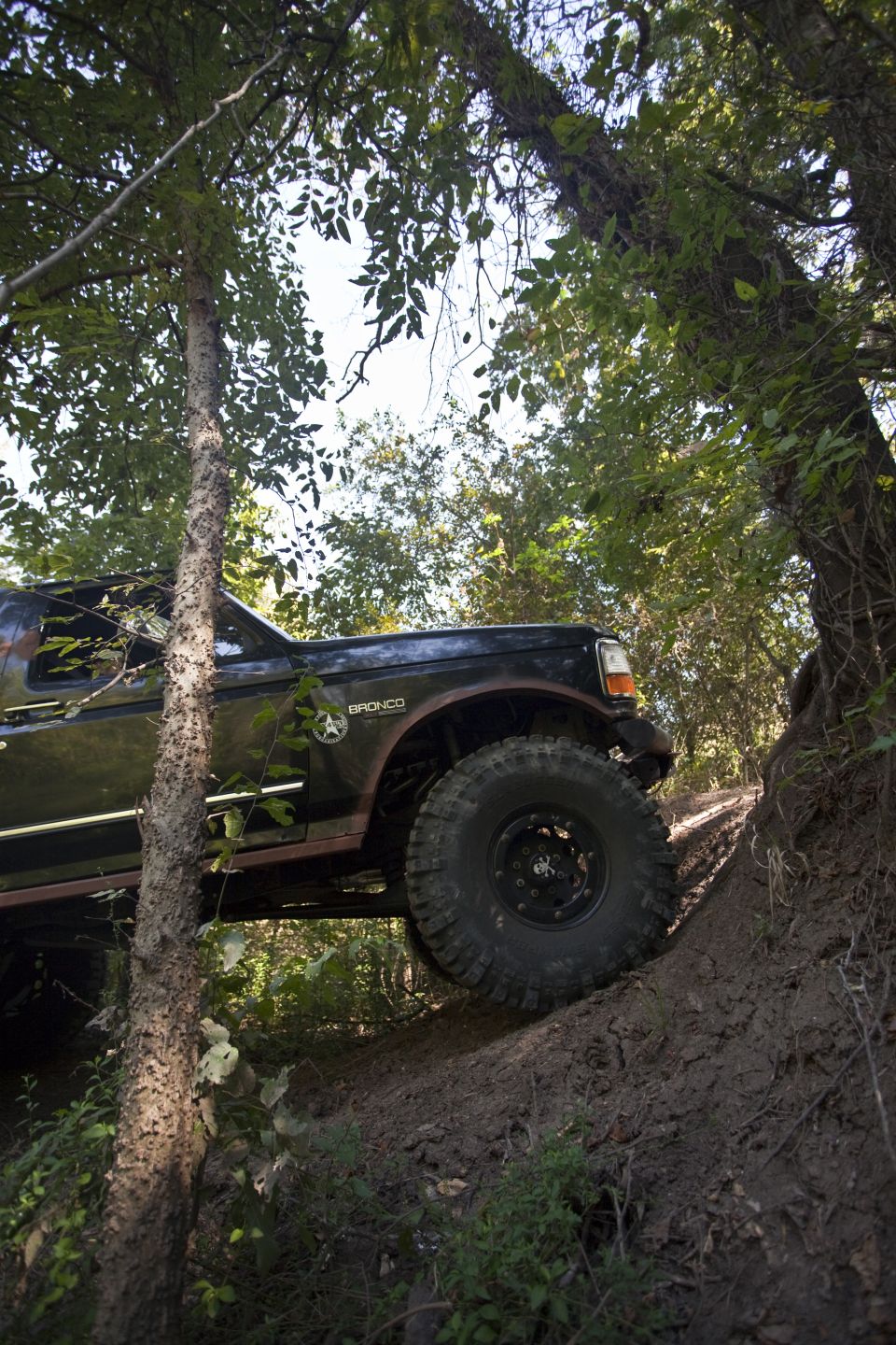 Black Ford Bronco on a dirt incline, side view, with large tires and off-road modifications