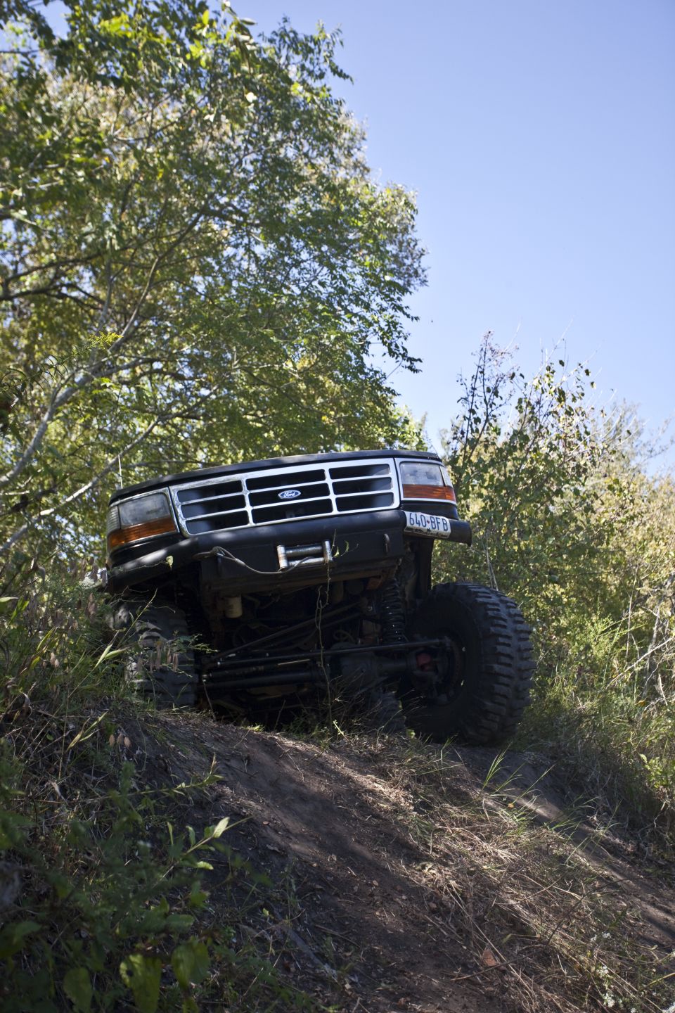 Black Ford Bronco on a dirt hill with large tires, front grille and headlights visible