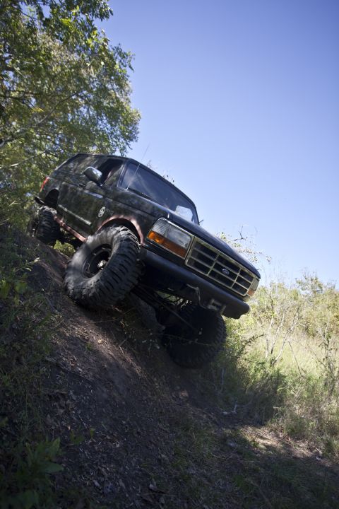 1995 Ford Bronco - This 1995 Ford Bronco is captured mid-climb on a steep, grassy incline under a clear blue sky.