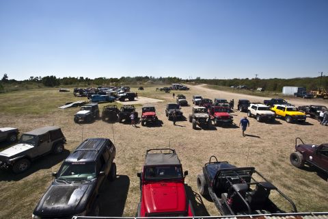 1995 Ford Bronco - A large gathering of off-road vehicles are parked in an open, dusty field on a sunny day.