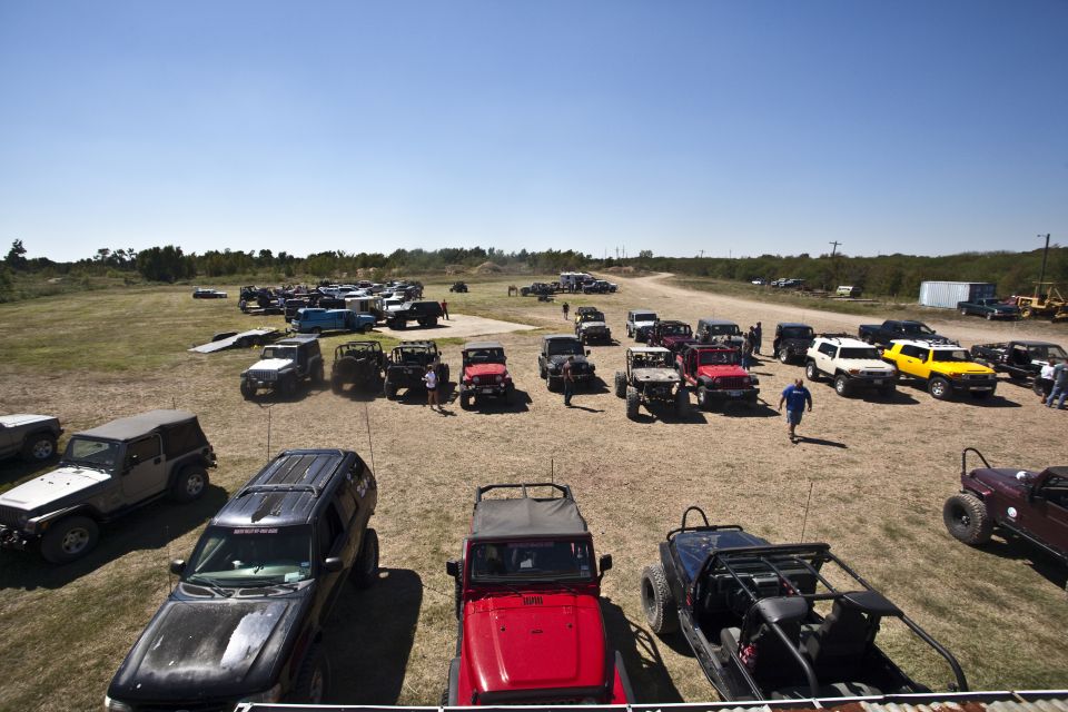 Many off-road vehicles, mostly Jeeps, parked in a dirt lot under a clear blue sky