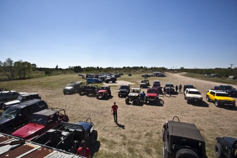 1995 Ford Bronco - A wide view of an outdoor gathering with numerous off-road vehicles parked on a dirt lot.