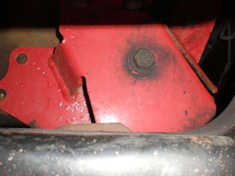 1995 Ford Bronco - Close-up of a red metal bracket with a bolt, likely a component of a vehicle's undercarriage.