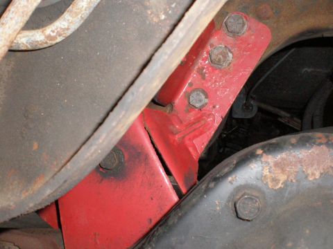 1995 Ford Bronco - Close-up view of a red painted bracket with bolts on a vehicle's undercarriage.