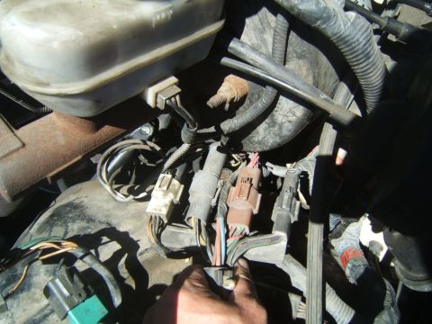1988 Ford Bronco - Close-up of an engine bay wiring harness with a hand disconnecting a connector.
