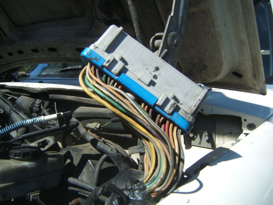 Engine control module with blue connector and bundle of colorful wires disconnected under a vehicle hood