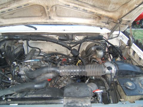 1988 Ford Bronco - The engine bay of a white vehicle, with visible hoses, wiring, and engine components. Text 'CAUTION FAN' is visible on a fan shroud.