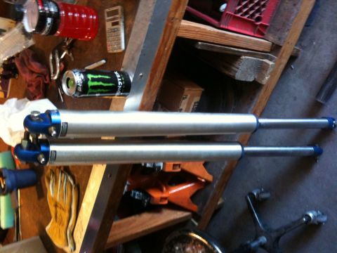 Suzuki Samurai - Pair of shock absorbers resting on a wooden shelf with tools and drinks.