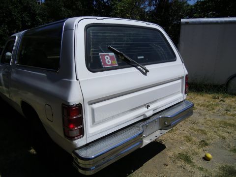 1987 Dodge 1500 - Rear view of a white 1987 Dodge 1500 SUV parked outdoors next to a trailer.