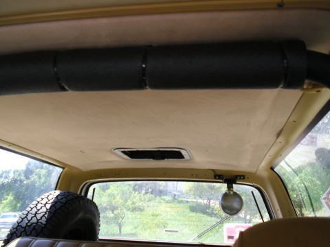 1987 Dodge 1500 - The interior of a vehicle shows a tan headliner, a black roll bar, and a spare tire mounted behind the seats.