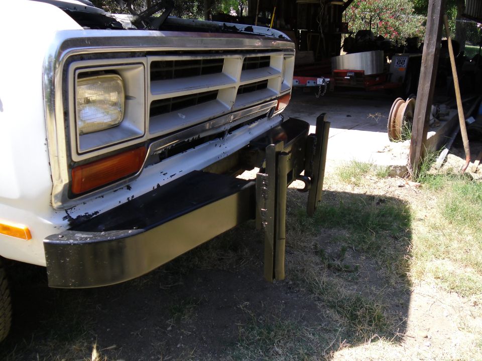 Front end of a white truck with a chrome grille and black bumper. Hood is open