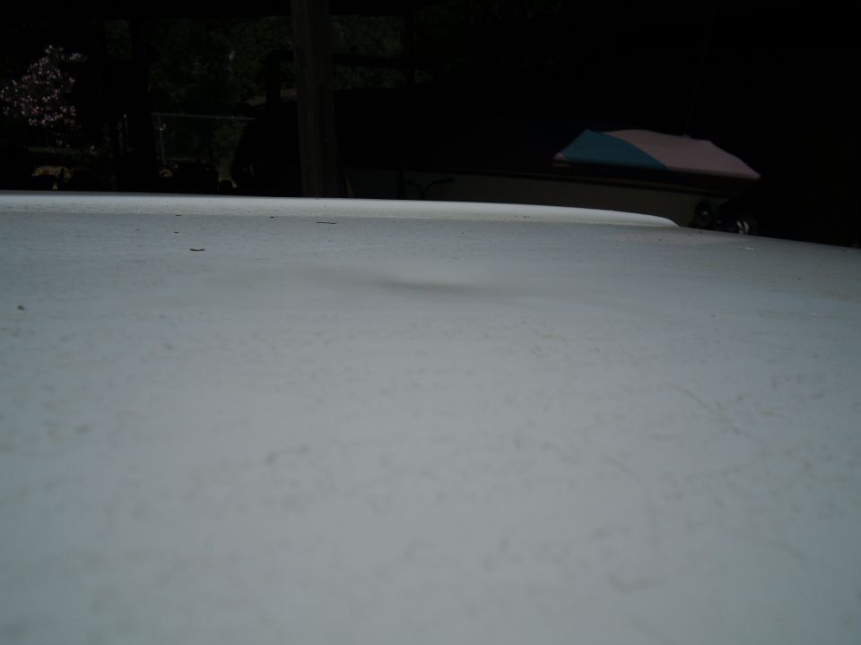 White truck bed with a dent, viewed from a low angle. A dark background with trees and a pole is visible