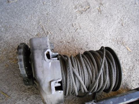 1987 Dodge 1500 - A winch mechanism is shown with its steel cable tightly wound around the drum, resting on a textured concrete ground.