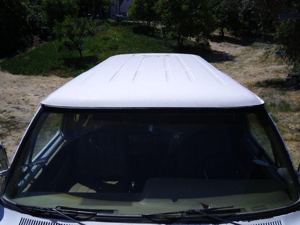 Top view of a white van's roof and windshield. The roof has several raised lines. The interior is dark