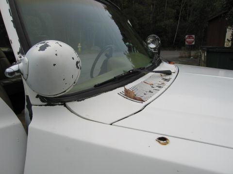 1987 Dodge 1500 - The front corner of a white truck shows wear and tear, with a damaged side mirror and a rusty spot on the hood.