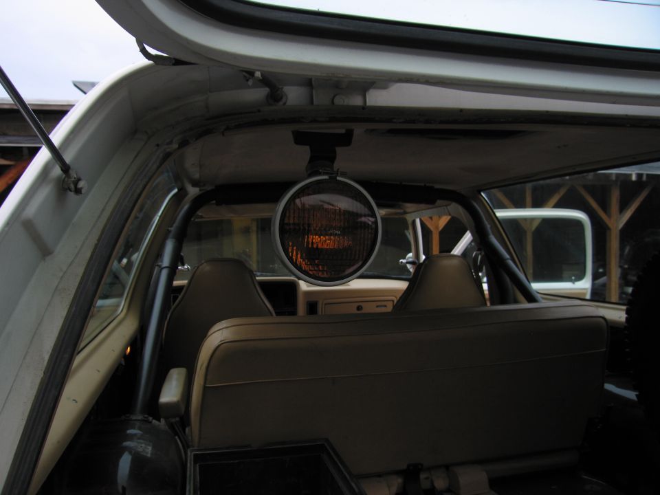 Interior view of a vehicle showing tan seats, a roll bar, and a mounted spotlight above the dashboard. Another vehicle is visible through the rear window