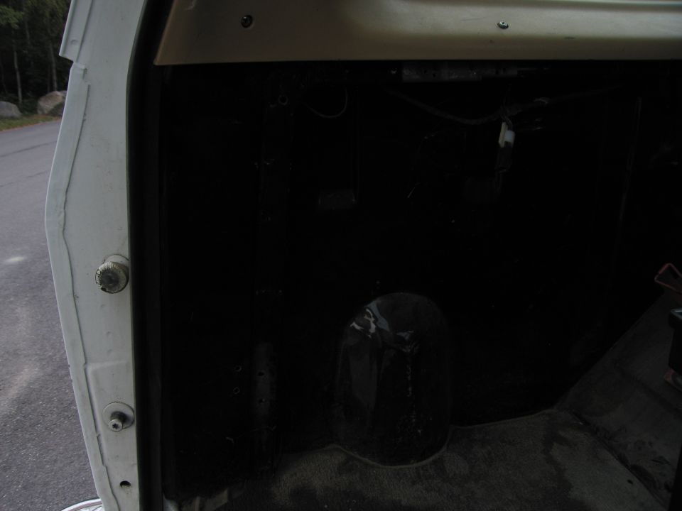 Interior of a white vehicle, showing the black floor and lower door jamb. A round hump is visible on the floor