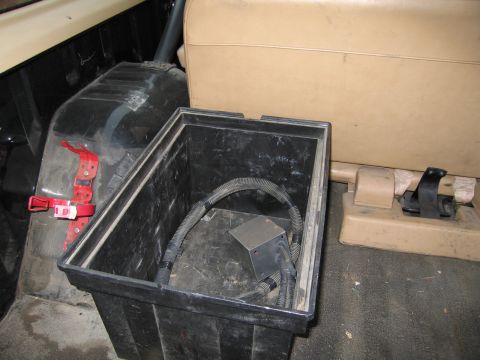 1987 Dodge 1500 - The interior of a vehicle is shown, a black storage bin containing electrical wiring and components, positioned next to tan seating.