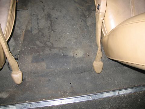 1987 Dodge 1500 - The interior floor of a vehicle shows tan seat bases and dark, worn carpet with some stains.