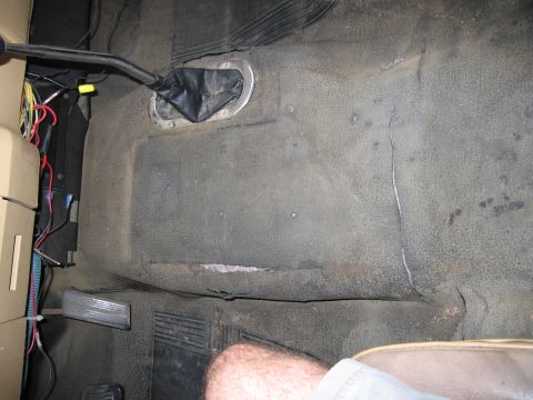 1987 Dodge 1500 - The worn floor of a vehicle's interior, with exposed wiring near the transmission tunnel and pedals.