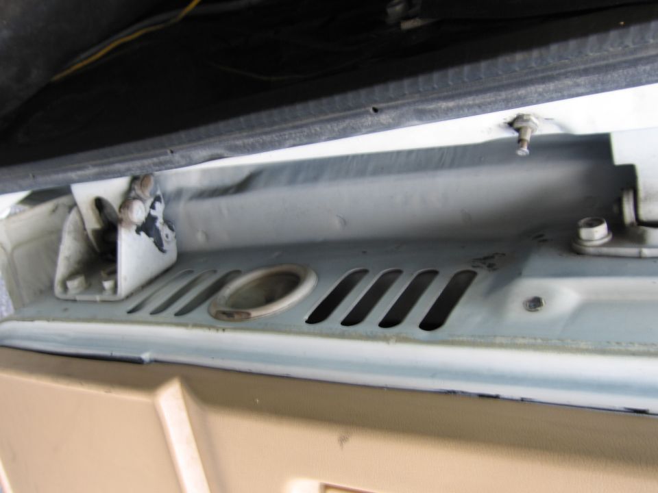 Close-up of a white vehicle's engine bay, showing a latch mechanism and slotted vents