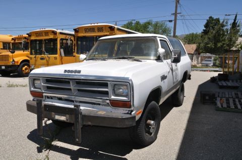 1987 Dodge 1500 - A white 1987 Dodge Ramcharger is parked in front of several yellow school buses.