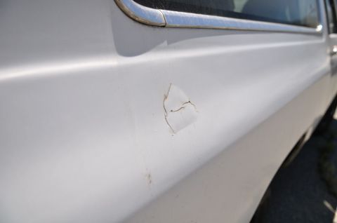 1987 Dodge 1500 - The side panel of a white vehicle shows damage with cracked paint and a small dent.
