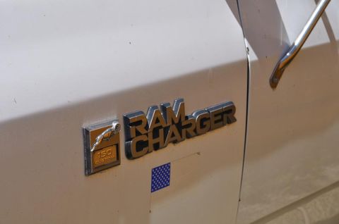 1987 Dodge 1500 - The Ramcharger emblem is visible on the side of a white vehicle, alongside a smaller badge indicating '150 Custom'.