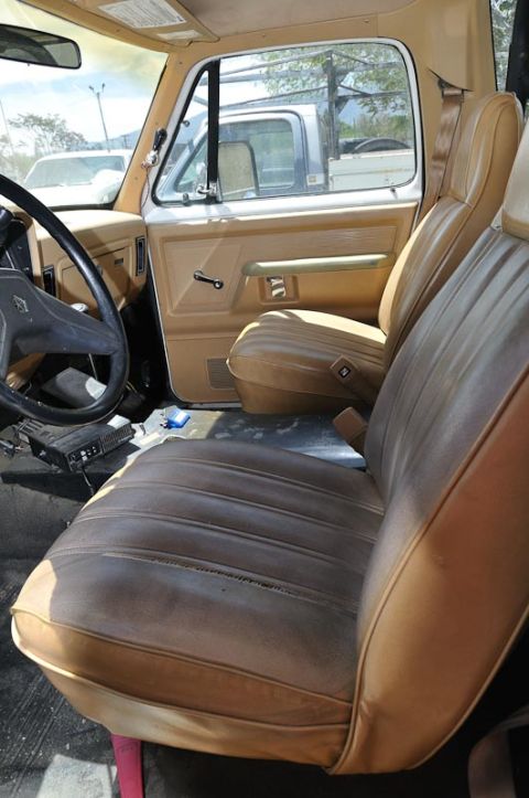 1987 Dodge 1500 - The interior of a 1987 Dodge 1500 pickup truck features tan vinyl seats and door panels, with another truck visible through the window.