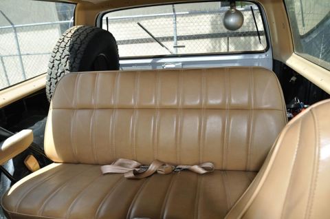1987 Dodge 1500 - The interior of a vehicle shows a tan bench seat with a seatbelt and a spare tire mounted behind it.