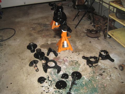 1979 Ford Bronco - Various black suspension components are laid out on a garage floor, some resting on orange jack stands.