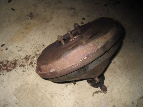 1979 Ford Bronco - A rusty brake booster sits on a concrete surface, showing signs of wear and age.