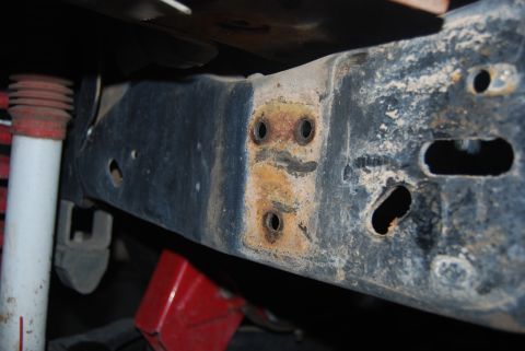 1982 Ford Bronco - Vehicle frame rail shows rust and mounting holes, with a shock absorber in view.