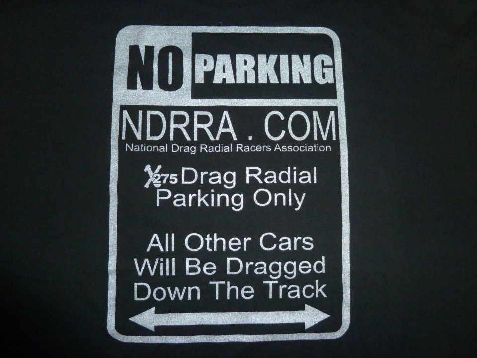 Sign with white text on black background: NO PARKING, NDRRA.COM, National Drag Radial Racers Association, 1/275 Drag Radial Parking Only, All Other Cars Will Be Dragged Down The Track, with double-headed arrow