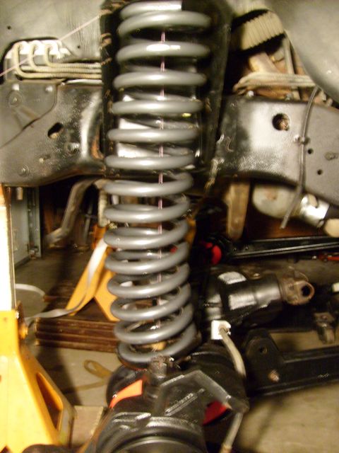 1986 Ford Bronco - Close-up of vehicle suspension components, including a gray coil spring and black metal parts, supported by yellow jack stands.