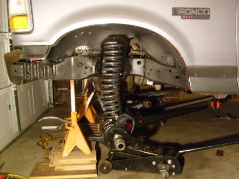 1986 Ford Bronco - The front suspension of a Ford Bronco is disassembled for repair, with the vehicle elevated on jack stands.