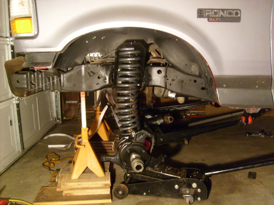 Ford Bronco XLT with front suspension removed, supported by jack stands and a floor jack