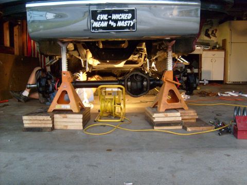 1986 Ford Bronco - Vehicle's rear axle and suspension are elevated on jack stands for maintenance, with a custom license plate visible.