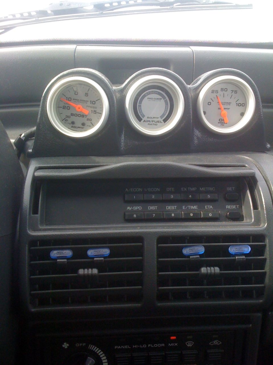 Car interior showing three gauges (boost, air/fuel, oil) above air vents and a radio