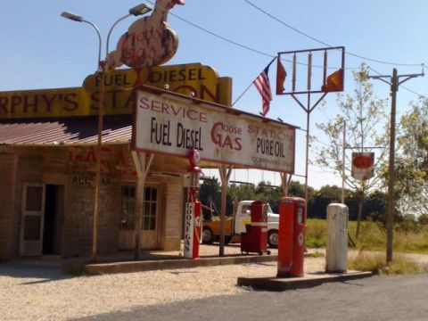 1991 Ford LTD Crown Victoria - A white truck is parked at a vintage gas station with a "Fuel Diesel" sign and a large duck decoration.