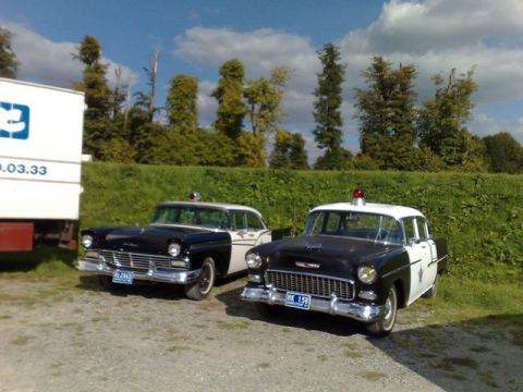 1991 Ford LTD Crown Victoria - Two vintage police cars, a 1955 Chevrolet and a mid-50s Ford, are parked outdoors on a sunny day.