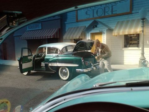 1991 Ford LTD Crown Victoria - A man loads items into the trunk of a green and white 1954 sedan parked in front of a store.