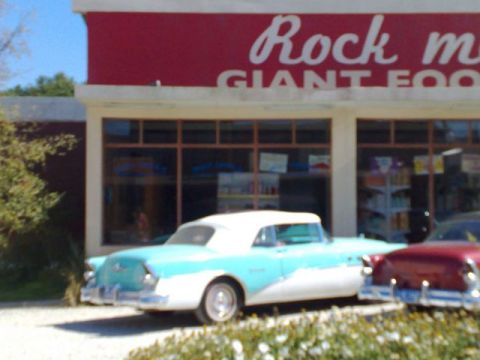 1991 Ford LTD Crown Victoria - Two vintage convertibles are parked in front of a store with a red sign.