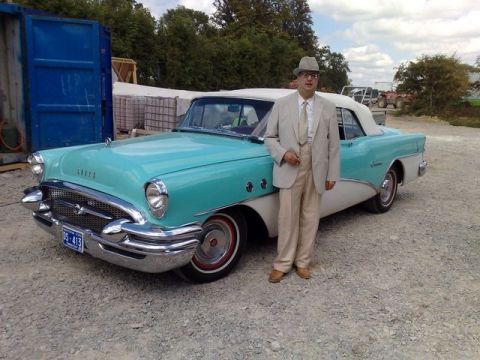 1991 Ford LTD Crown Victoria - A man in a light-colored suit and hat poses next to a classic two-tone Buick convertible.