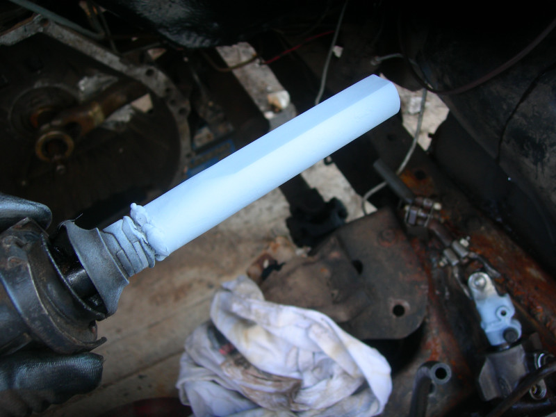 Close-up of a light blue painted steering column shaft being held, with vehicle parts and a rag in the background