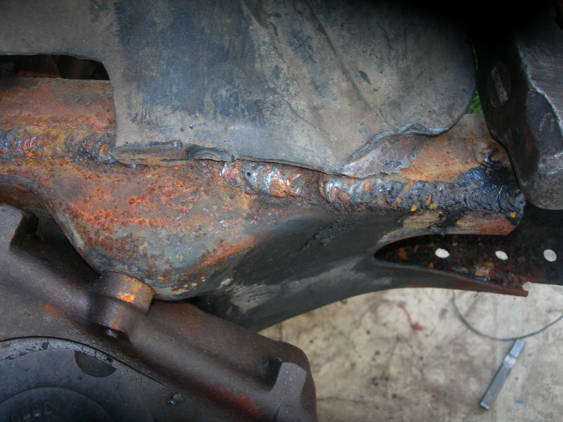 close-up of rusted frame section with visible welds and some black undercoating