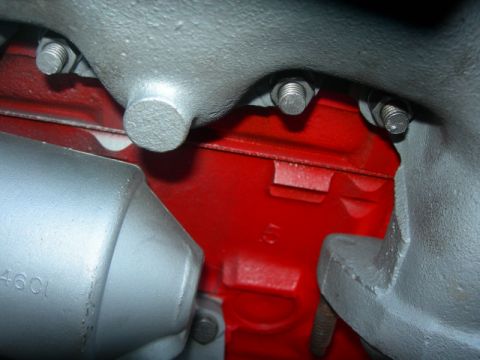 1984 Ford Bronco - Close-up view of an engine block, painted red, with various bolted metal parts and some visible part numbers.