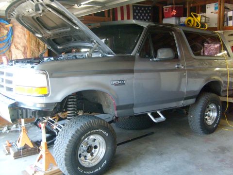1986 Ford Bronco - This Ford Bronco is undergoing maintenance in a garage, with its hood raised and front end supported by jack stands.