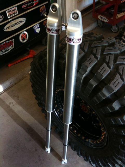 Suzuki Samurai - Pair of "HIGH HORN" shock absorbers and a large tire are shown in a garage setting.