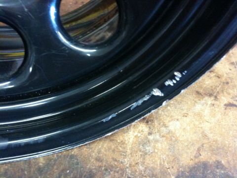2009 Suzuki Samurai - Close-up of a damaged black alloy wheel, showing scrapes and chipped paint on the outer edge.